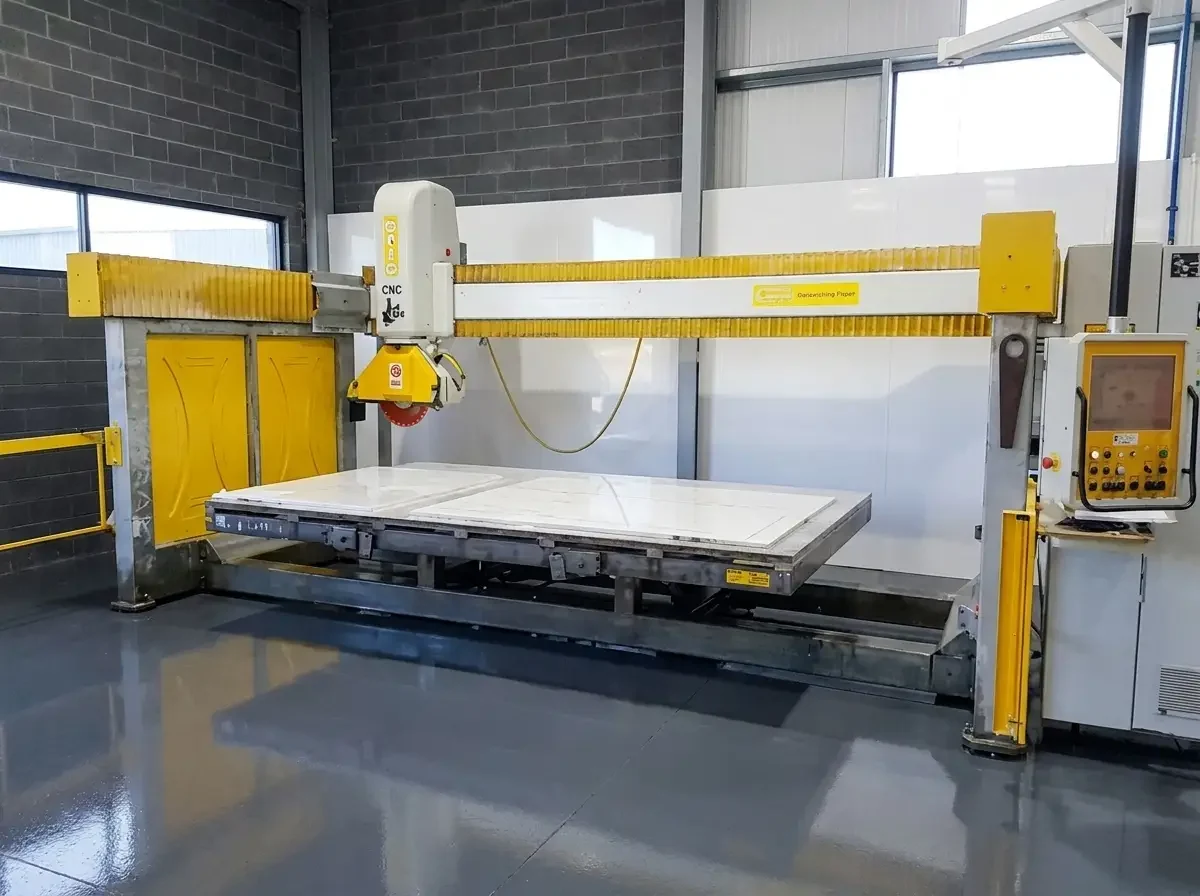 Bridge saw and control station above a stone slab in a fabrication shop